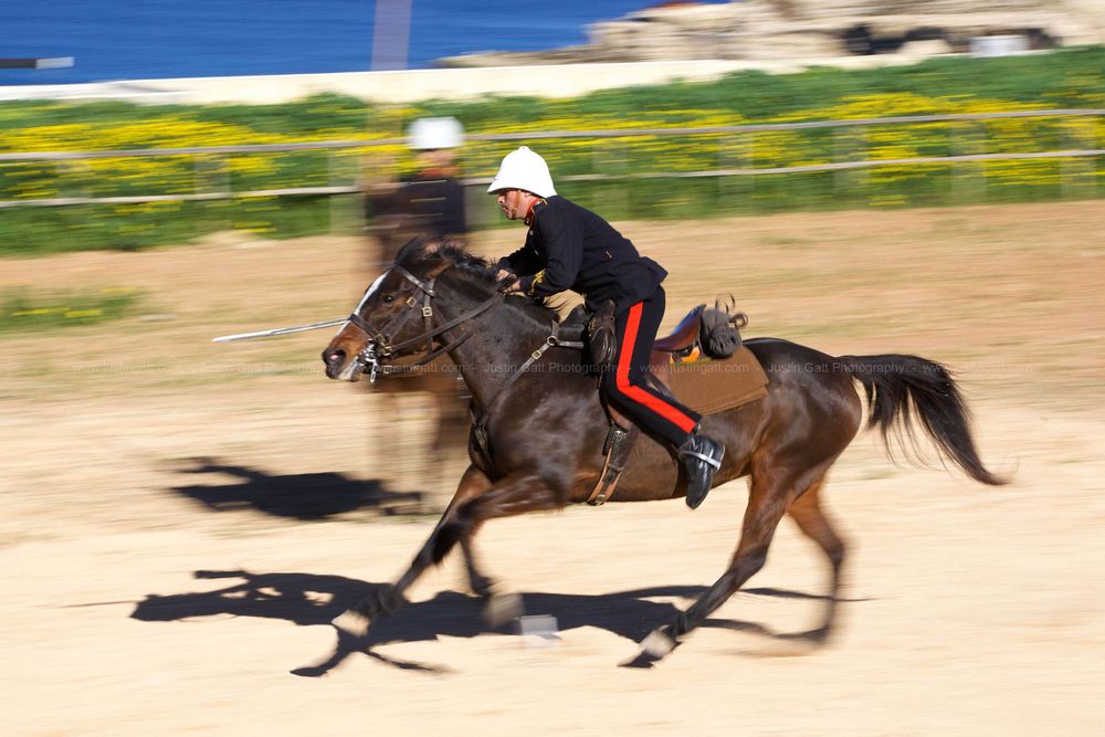 Sequence of horses and riders racing across a dirt track in motion blur.