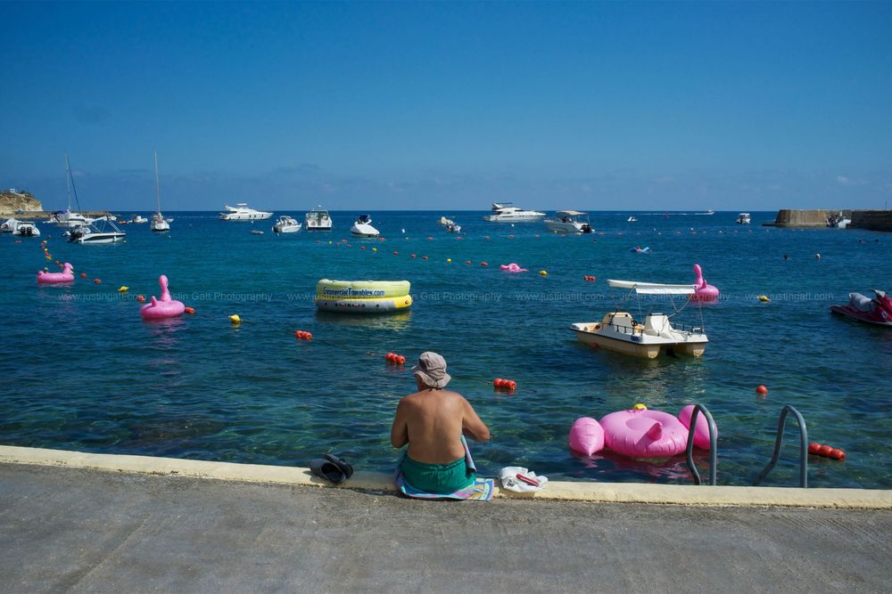 Panoramic view of a beach with colorful floats and boats dotting the blue ocean waters.