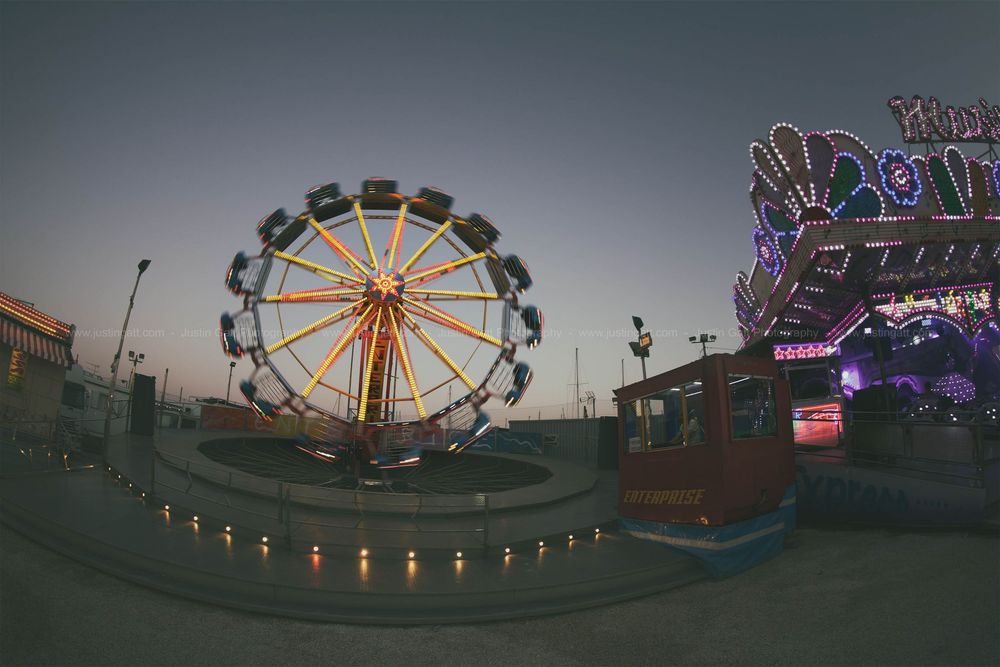 Carnival rides and ferris wheel silhouetted against dusky sky at an amusement park.