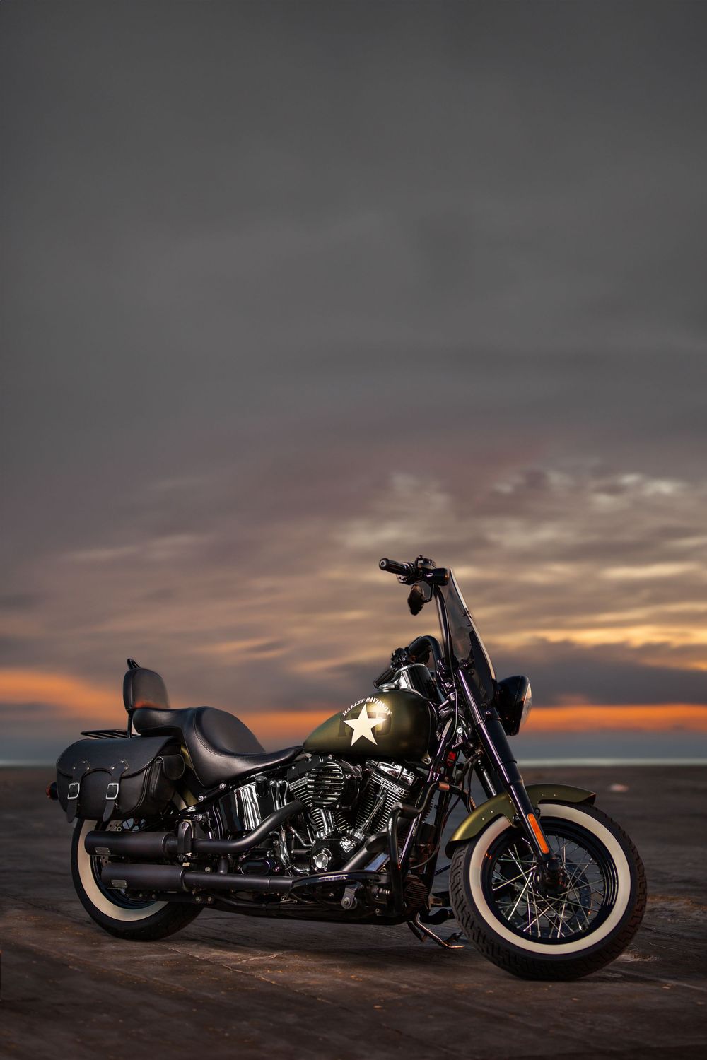Custom black motorcycles parked on desert terrain against a dramatic sunset sky.