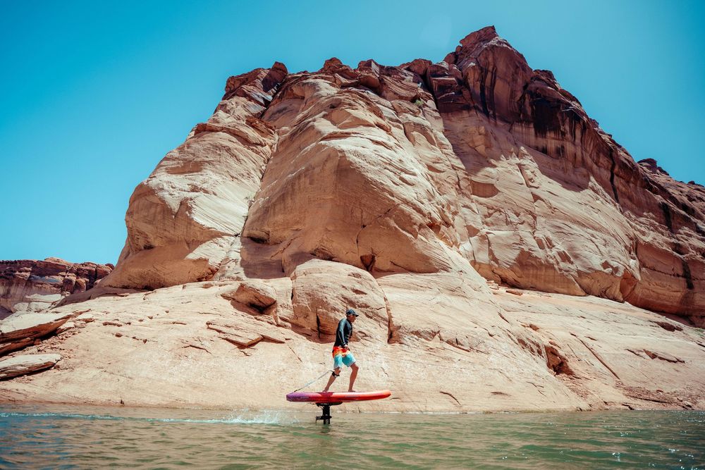 Stand up paddleboarder floats on calm water near towering red rock formations at Lake Powell.