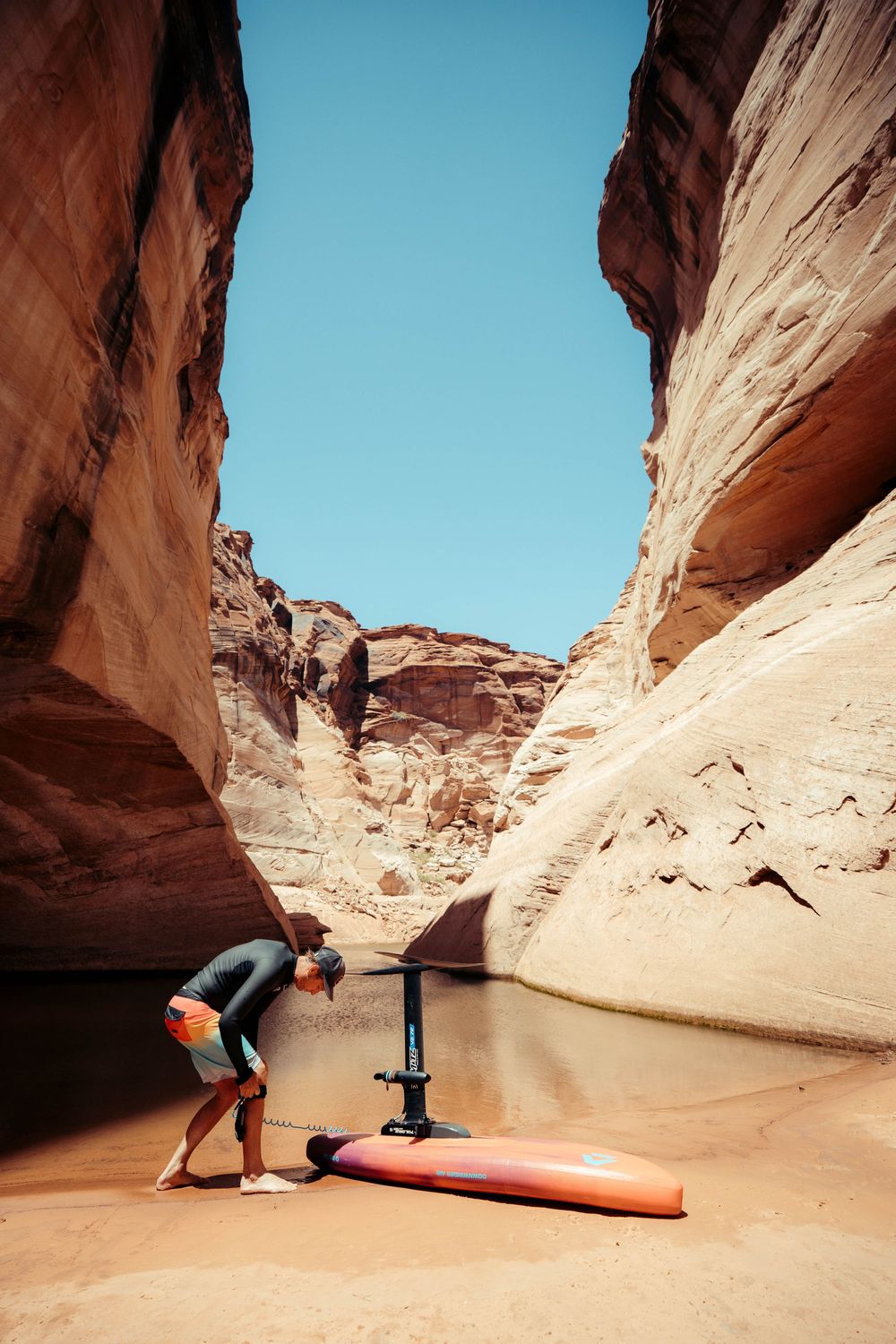 Person inflating a paddleboard in a narrow canyon with red rock walls and water at Lake Powell.