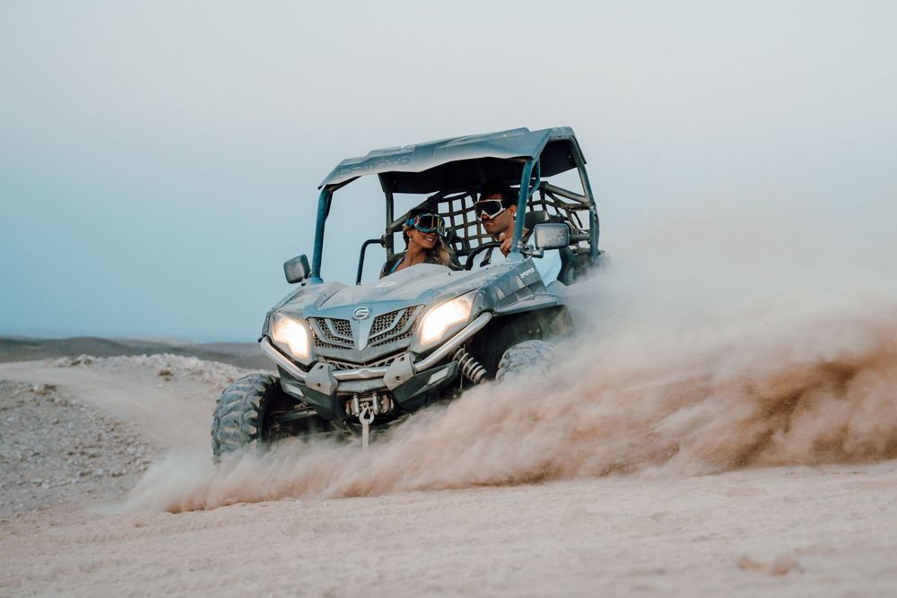 Off-road vehicle kicks up sand and dust while driving through desert terrain in dramatic action sequence.