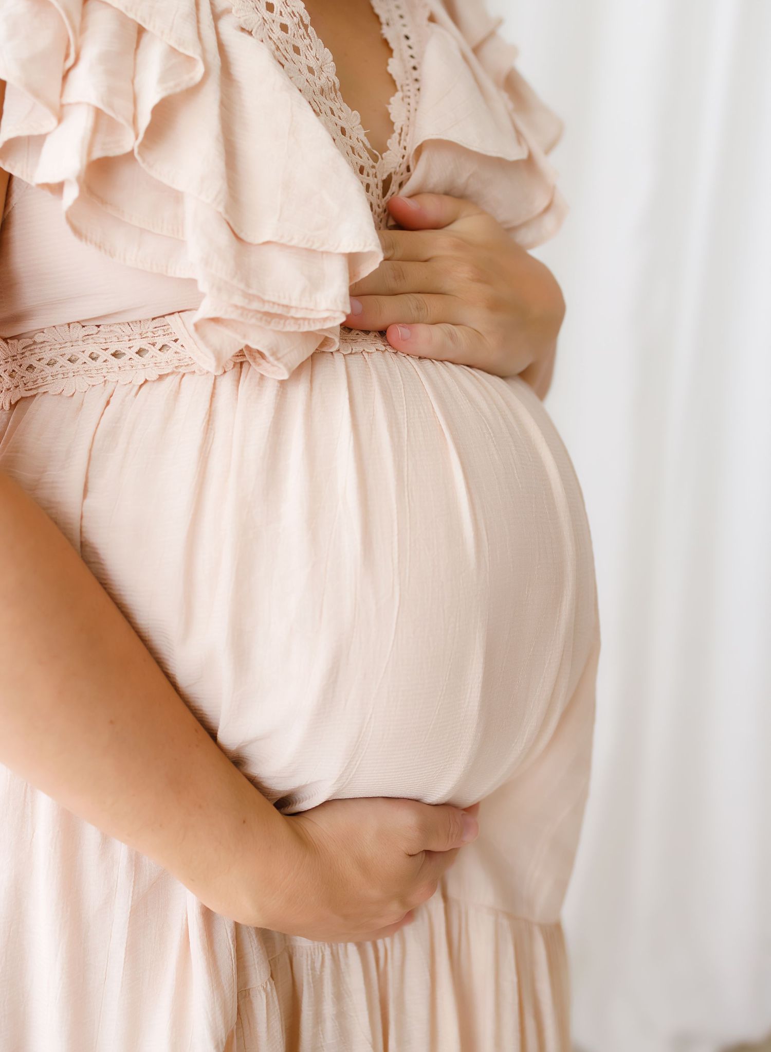Close up of pregnant woman's belly in soft pink lace maternity dress.