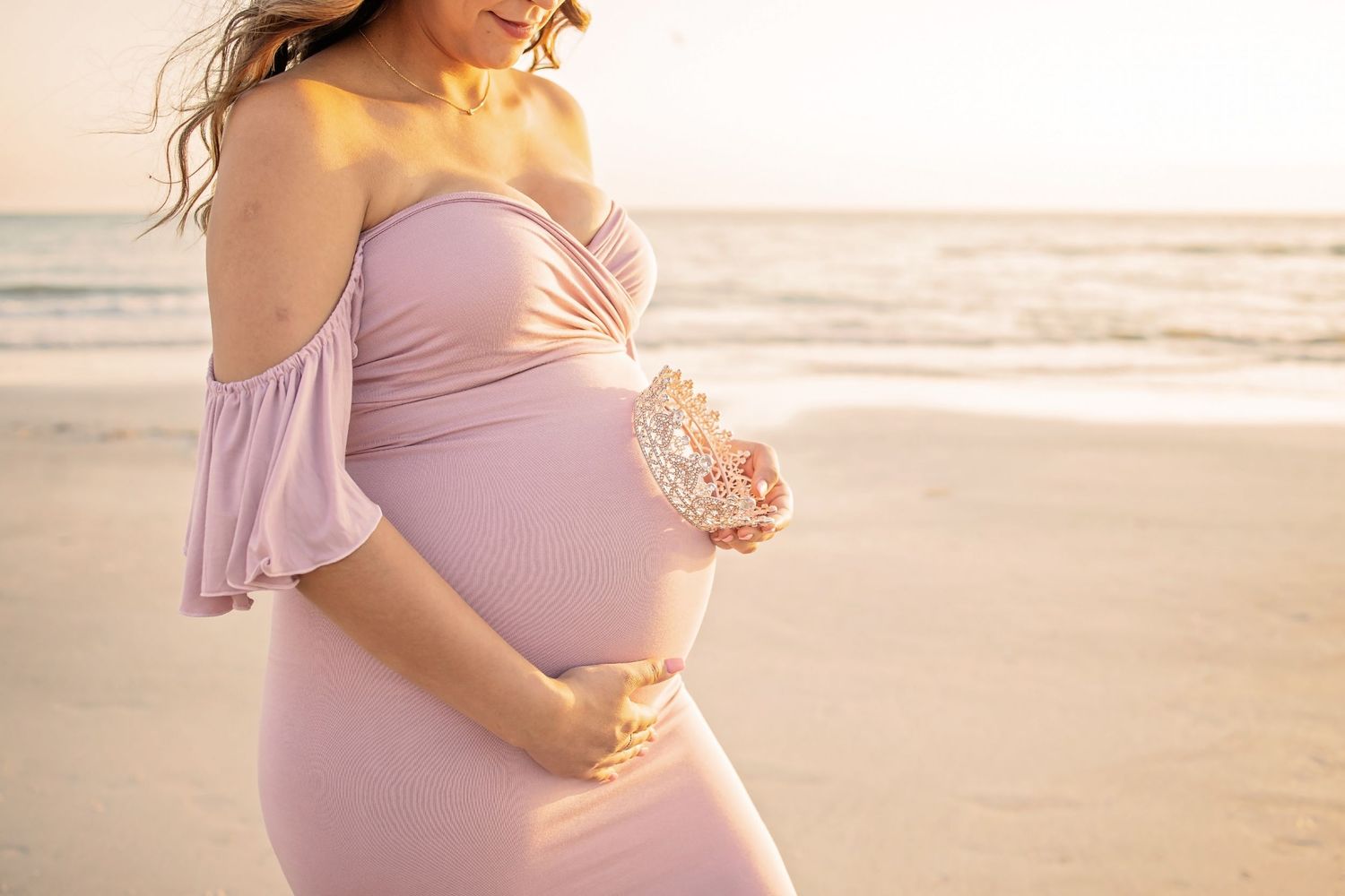 Close up of pregnant woman's belly in soft pink lace maternity dress.