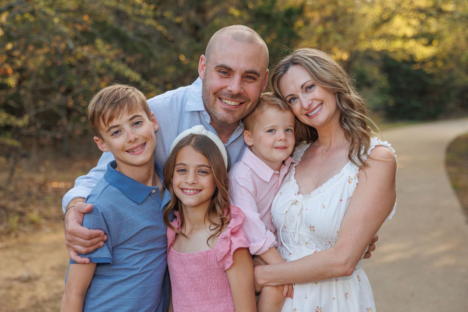 Family group wearing coordinated blue and pink outfits poses together outdoors during golden hour sunset.