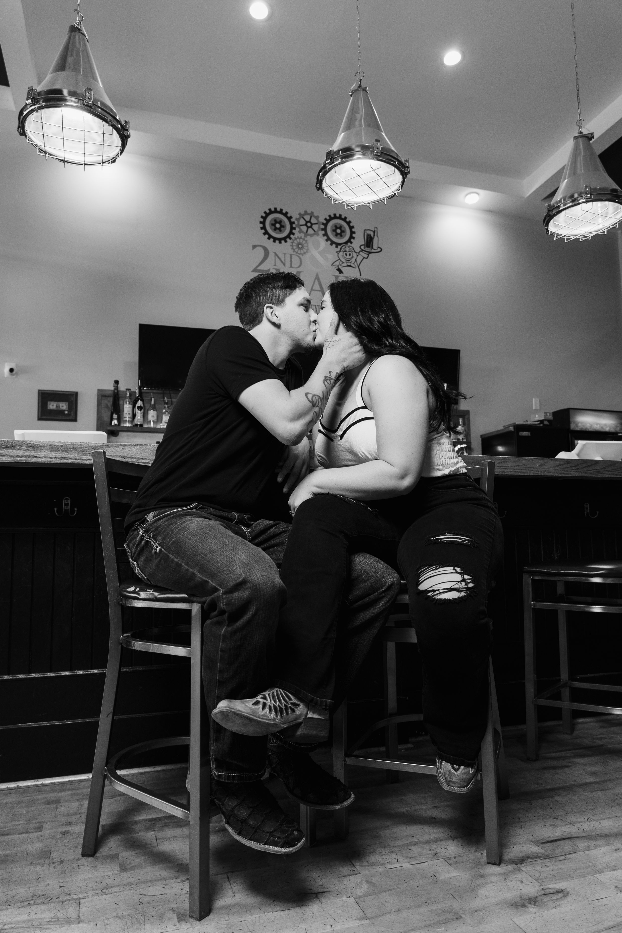 A couple shares intimate moments in a dimly lit indoor setting with pendant lights.