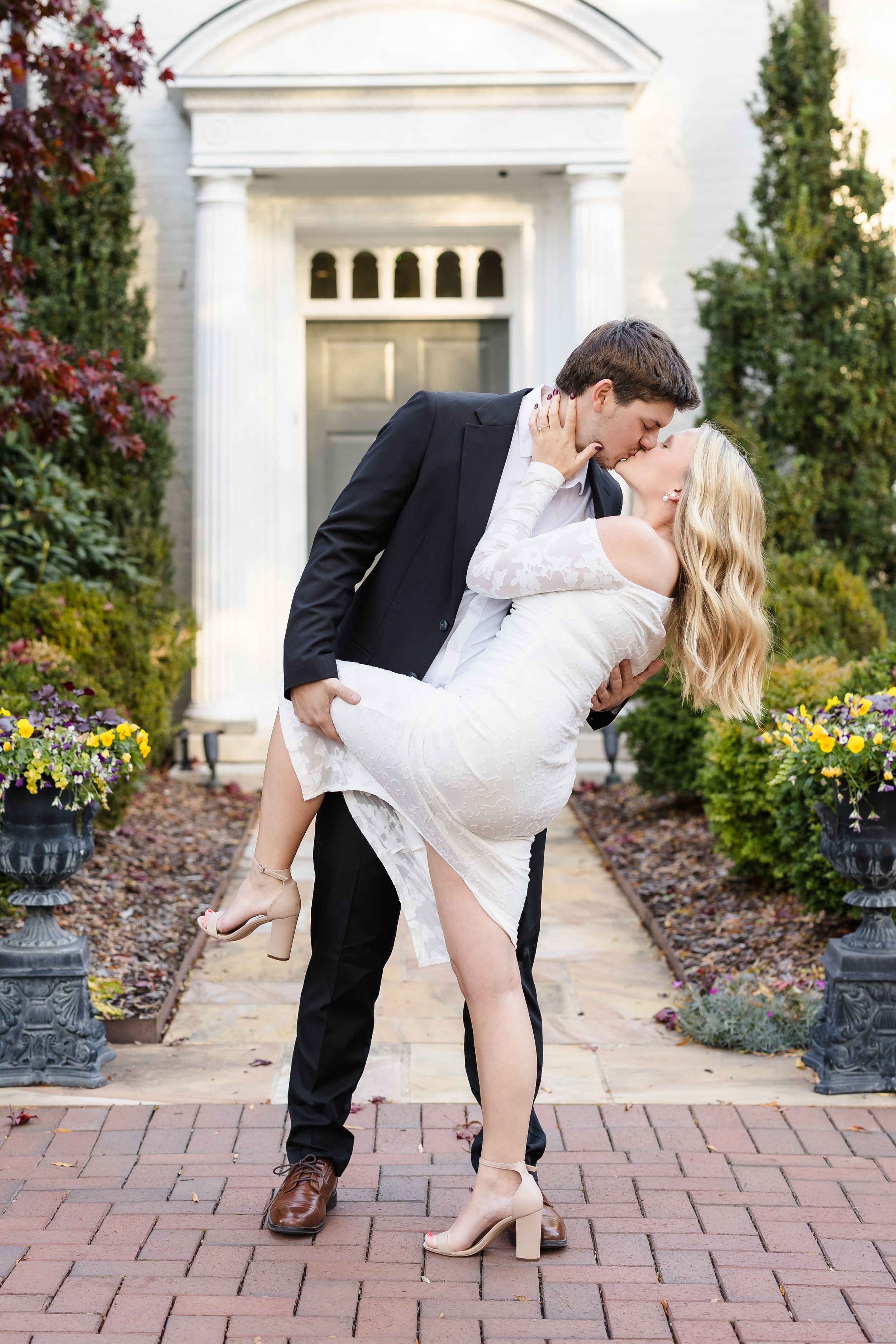 Romantic couple in formal attire dancing and dipping on a brick pathway near white columns.