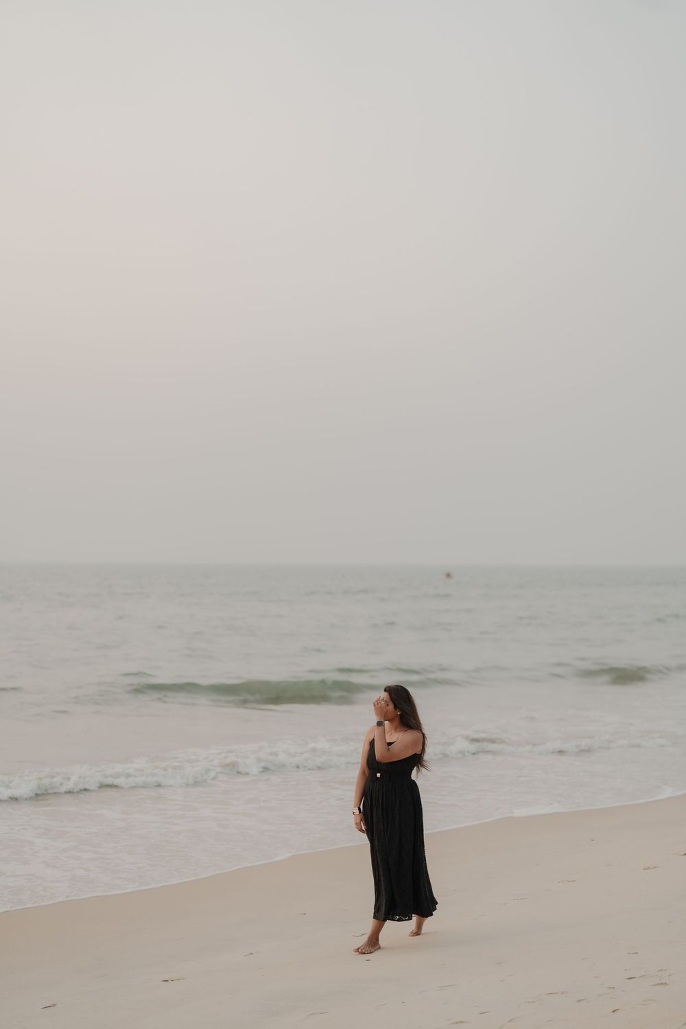 A couple shares intimate moments on a misty beach with soft overcast lighting and gentle waves in the background.