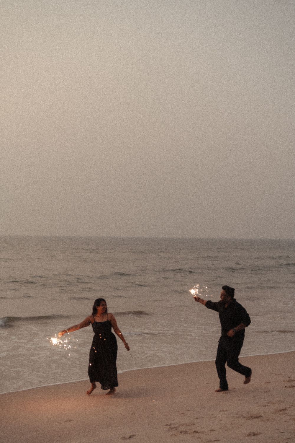 Silhouetted figures playing with sparklers on a misty beach at dusk create a dreamy sequence of motion.