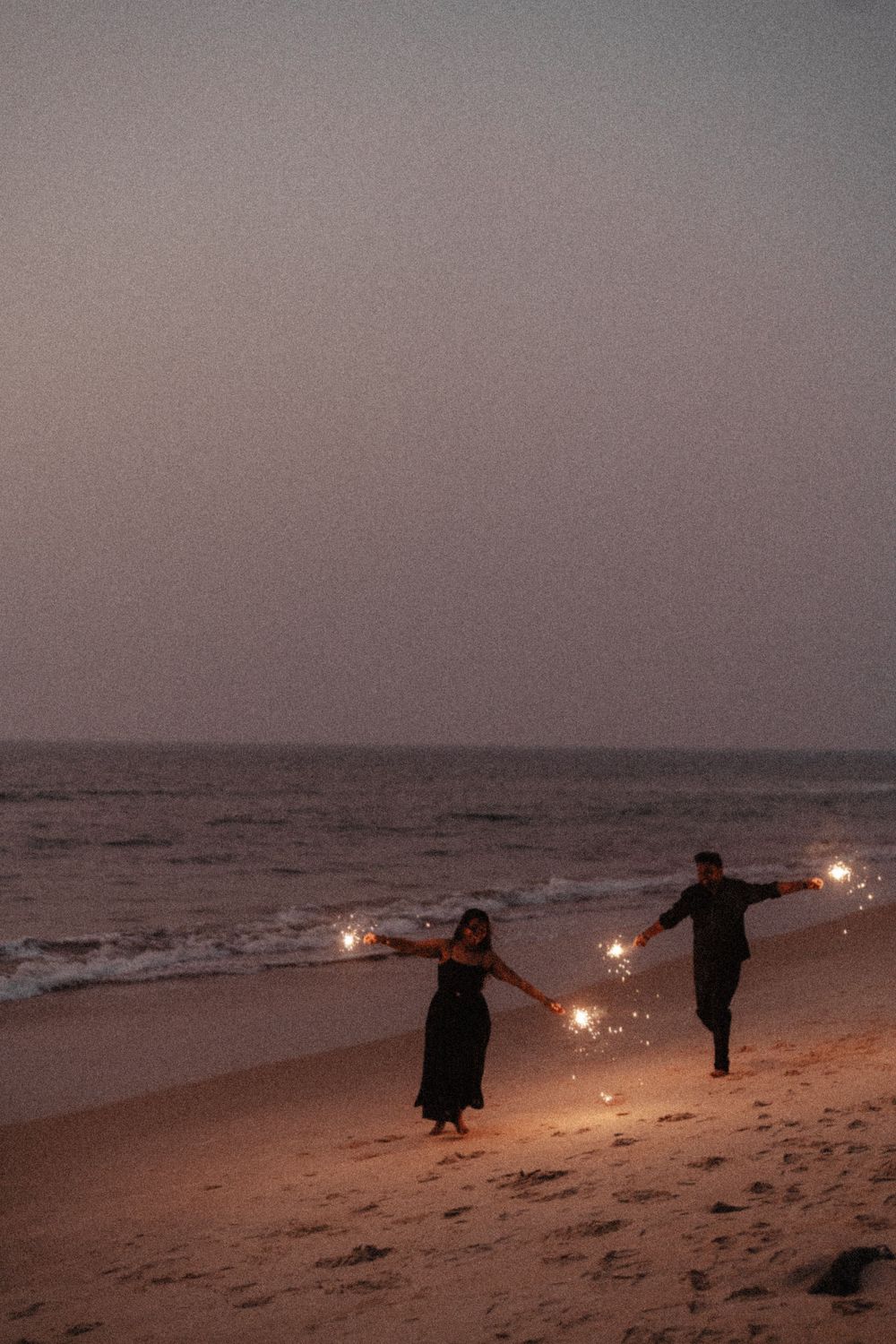 People holding sparklers create a magical twilight scene along the shoreline.
