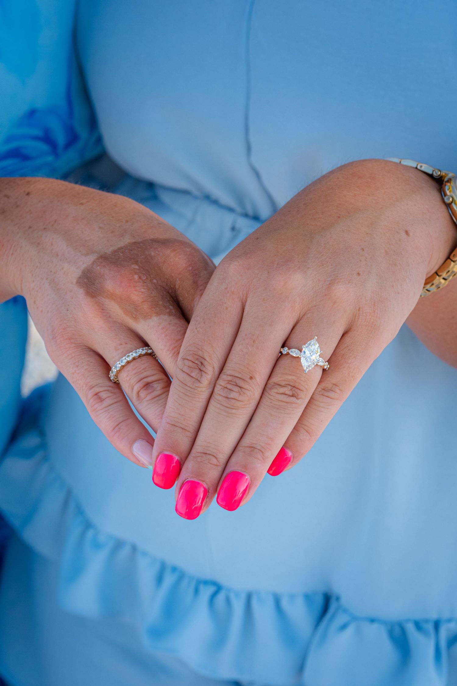 Close-up sequence of hands showing off an engagement ring with bright pink nail polish against a light blue background.