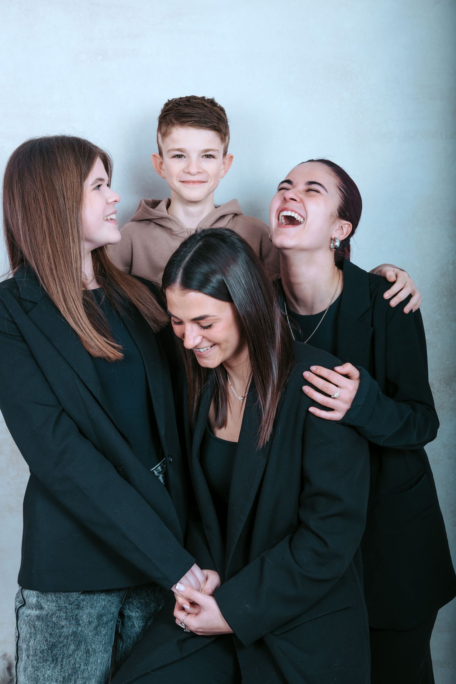A group of friends in black sweaters share a candid moment of laughter against a light blue wall.