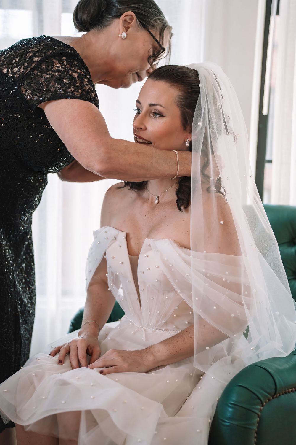 Intimate getting ready moment in a bridal suite with a teal chair and white dress.