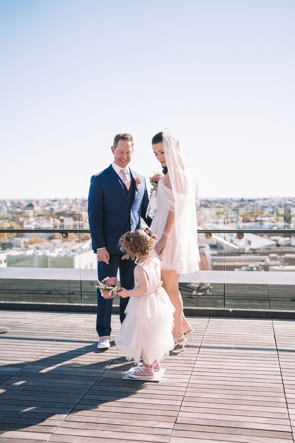 Wedding party on a rooftop terrace overlooking a cityscape on a sunny day.