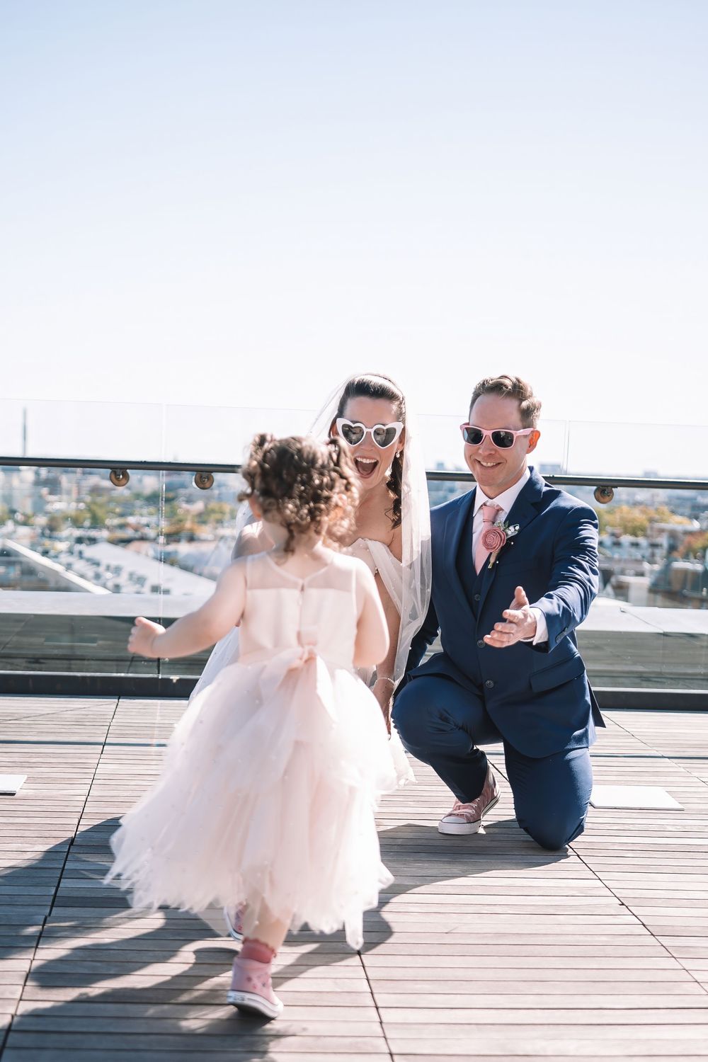 Playful couple in formal attire posing on a sunny rooftop terrace.