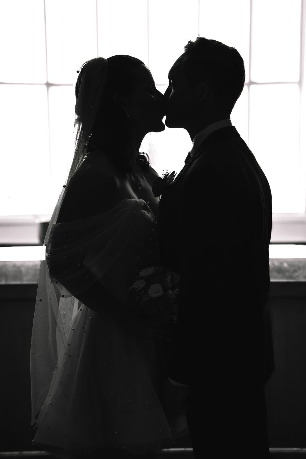 Silhouetted couple sharing romantic moments against bright window backdrop.
