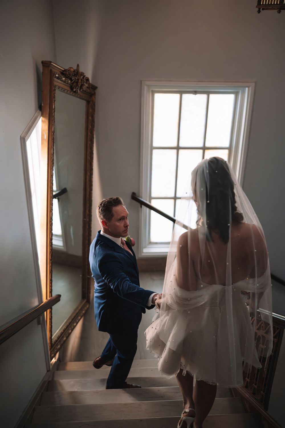 Artistic wedding photography sequence in a bright stairwell with dramatic lighting.