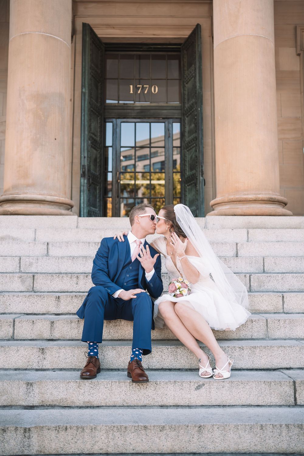 Wedding couple posing playfully on grand stone steps of historic building.