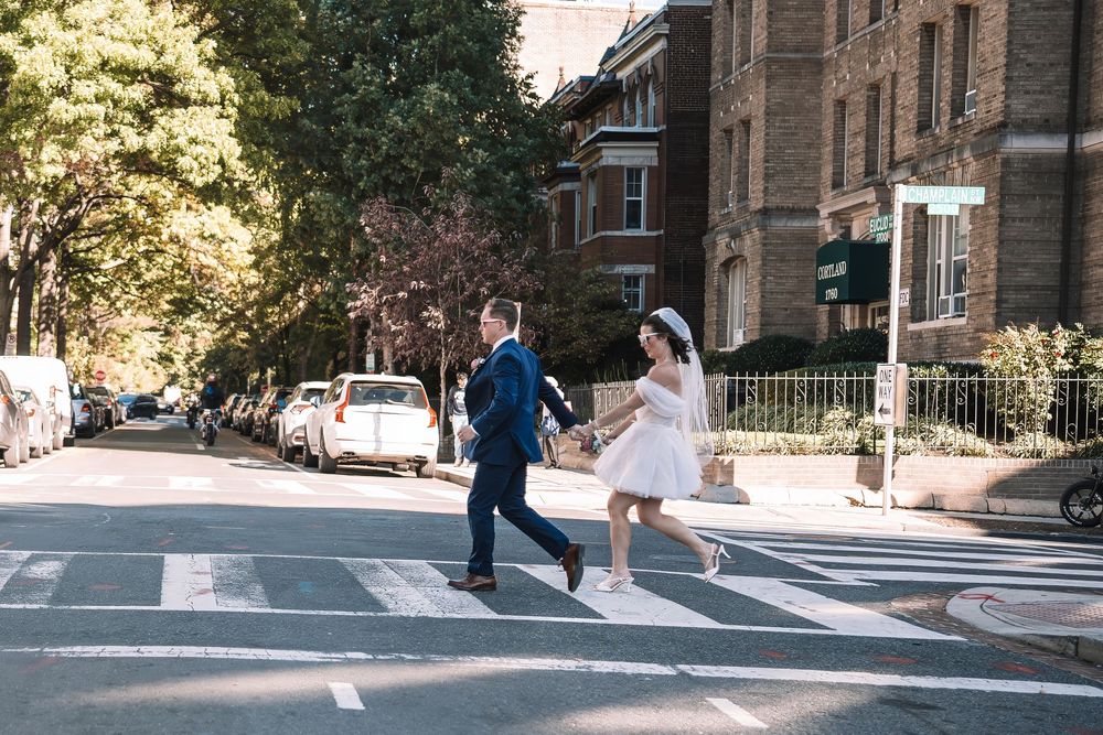 Wedding couple walking through tree-lined city street on sunny day.