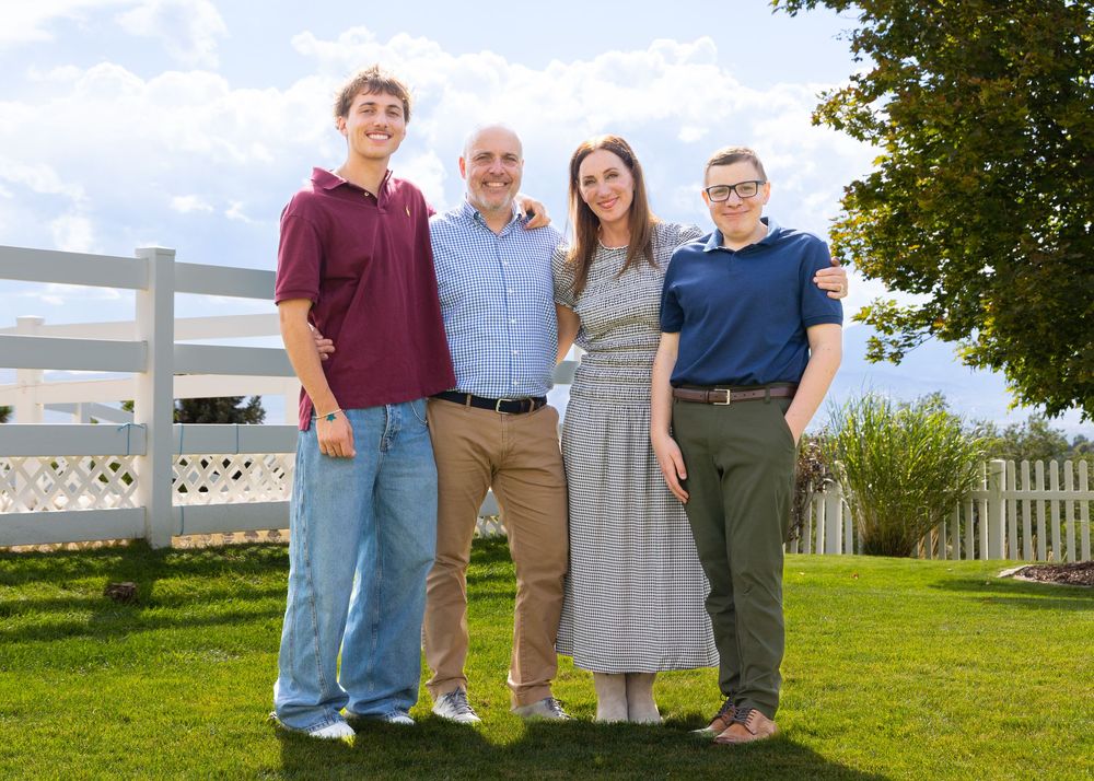 Outdoor family photos taken on a grassy hill with white picket fence in background.
