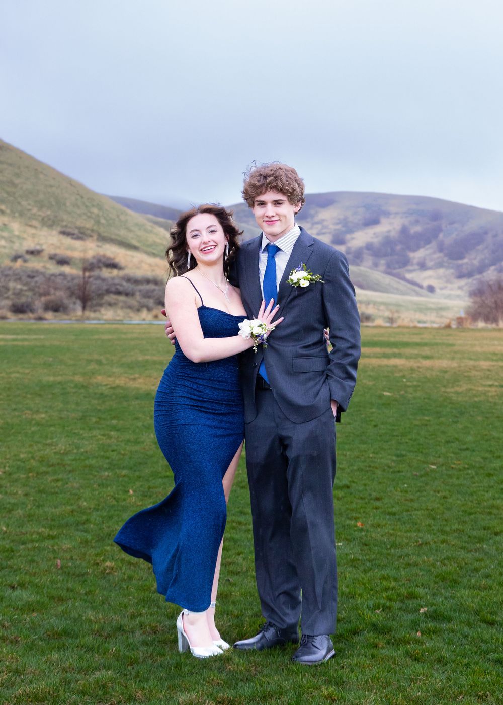 Formal couple photos in blue dress and suit on green hillside.