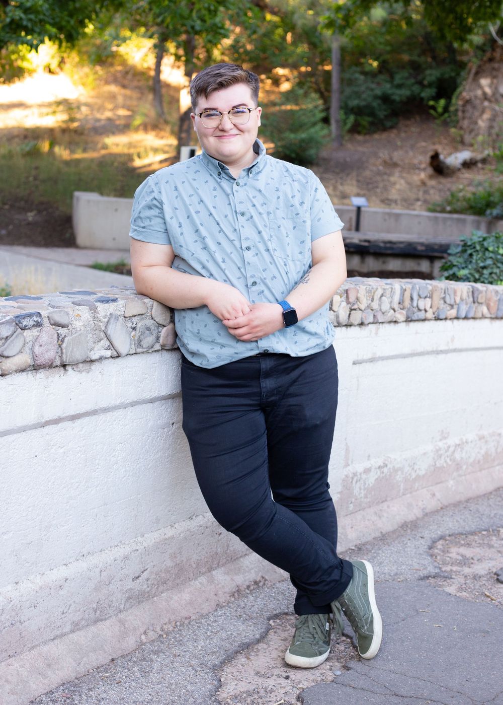Person sitting on stone wall wearing blue shirt and dark pants.