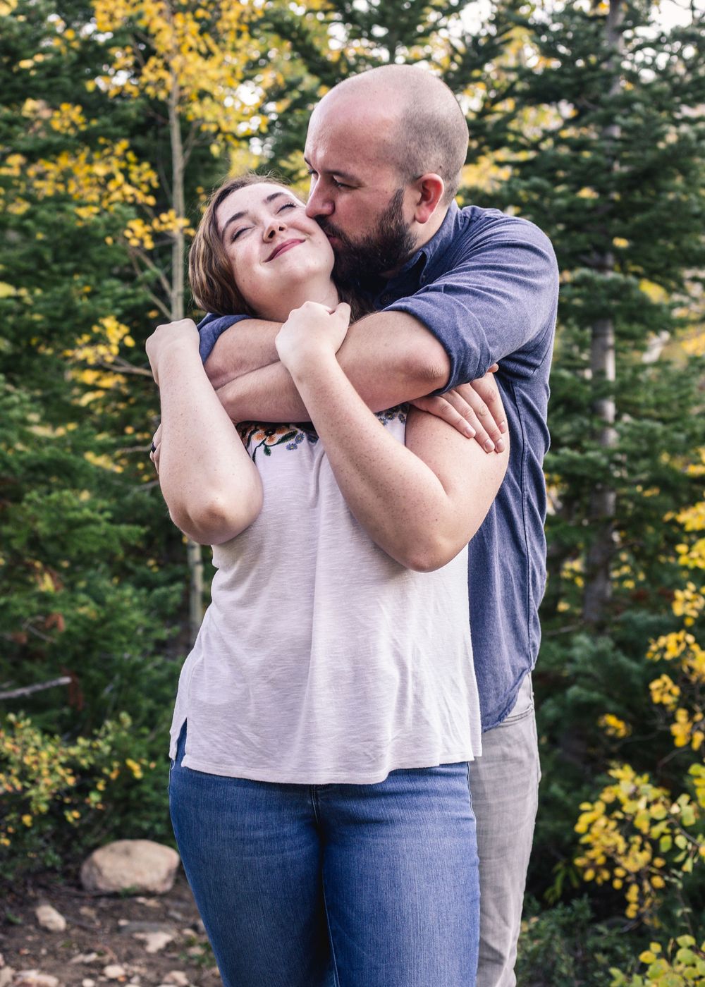 Couple embracing outdoors with fall foliage in background.