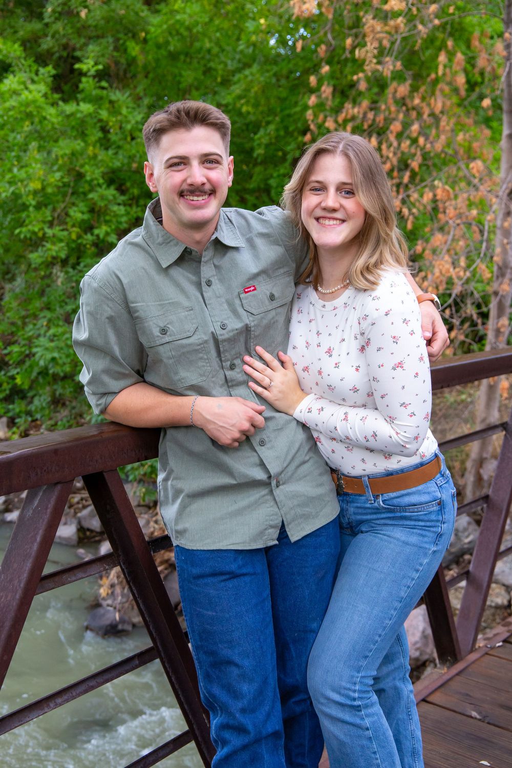 A couple poses together on a wooden bridge surrounded by lush greenery.