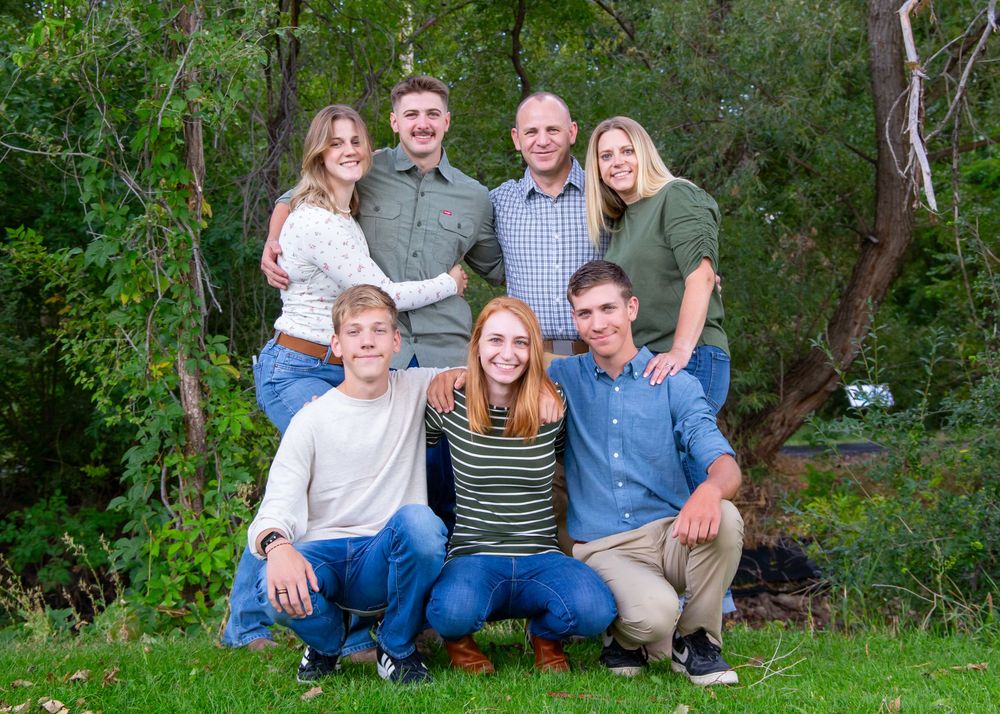 Family group sitting casually together on grass with trees in background.