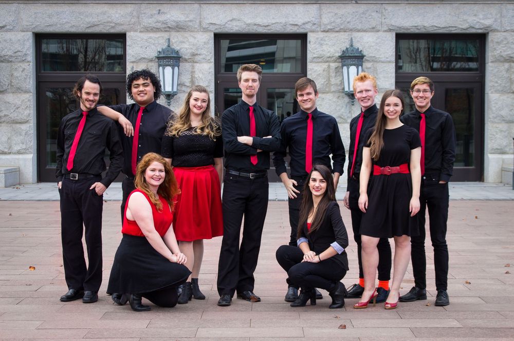 Performance group in black and red formal attire posing together on stone steps.