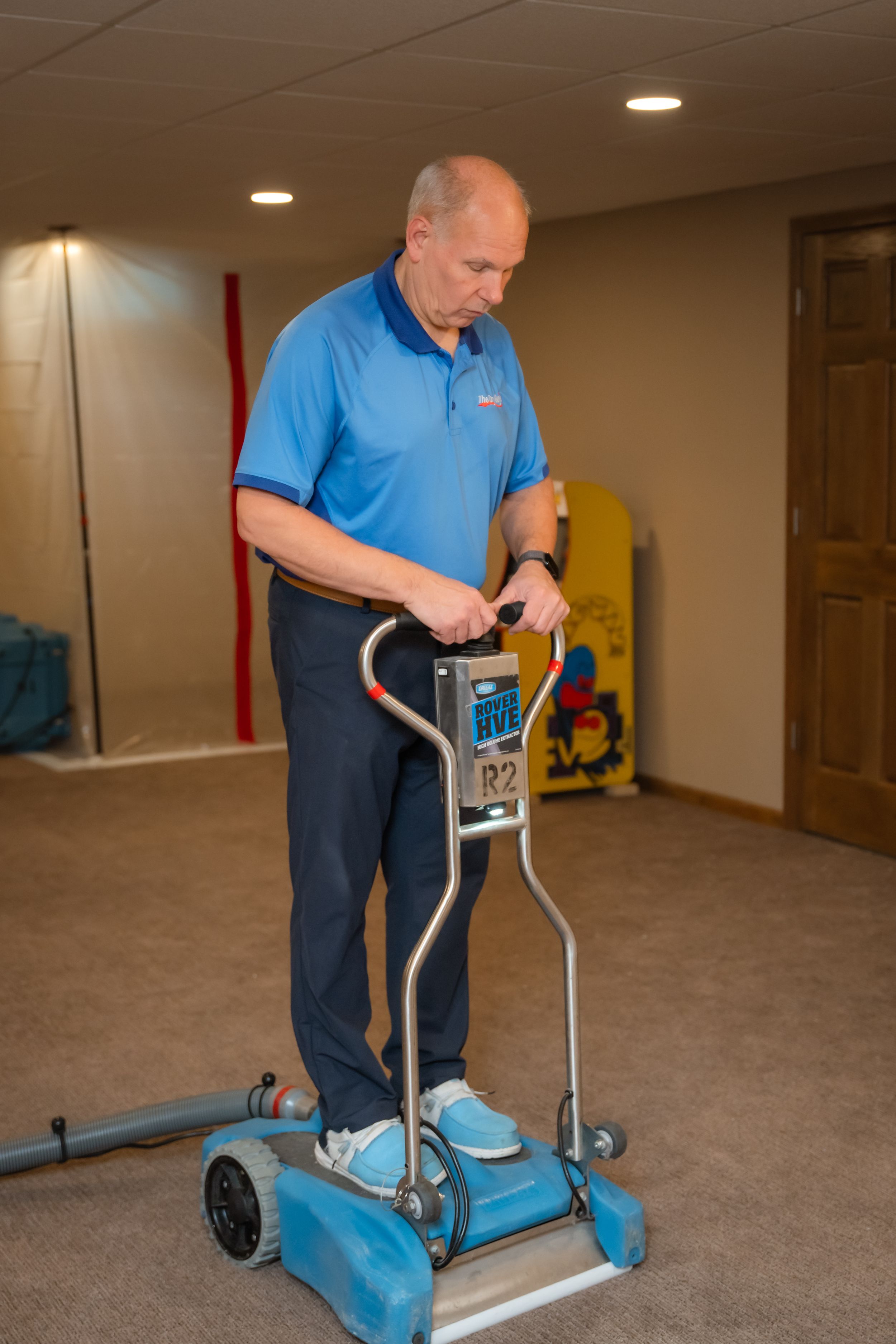 Person in blue shirt demonstrating use of an elliptical exercise machine in a carpeted room.