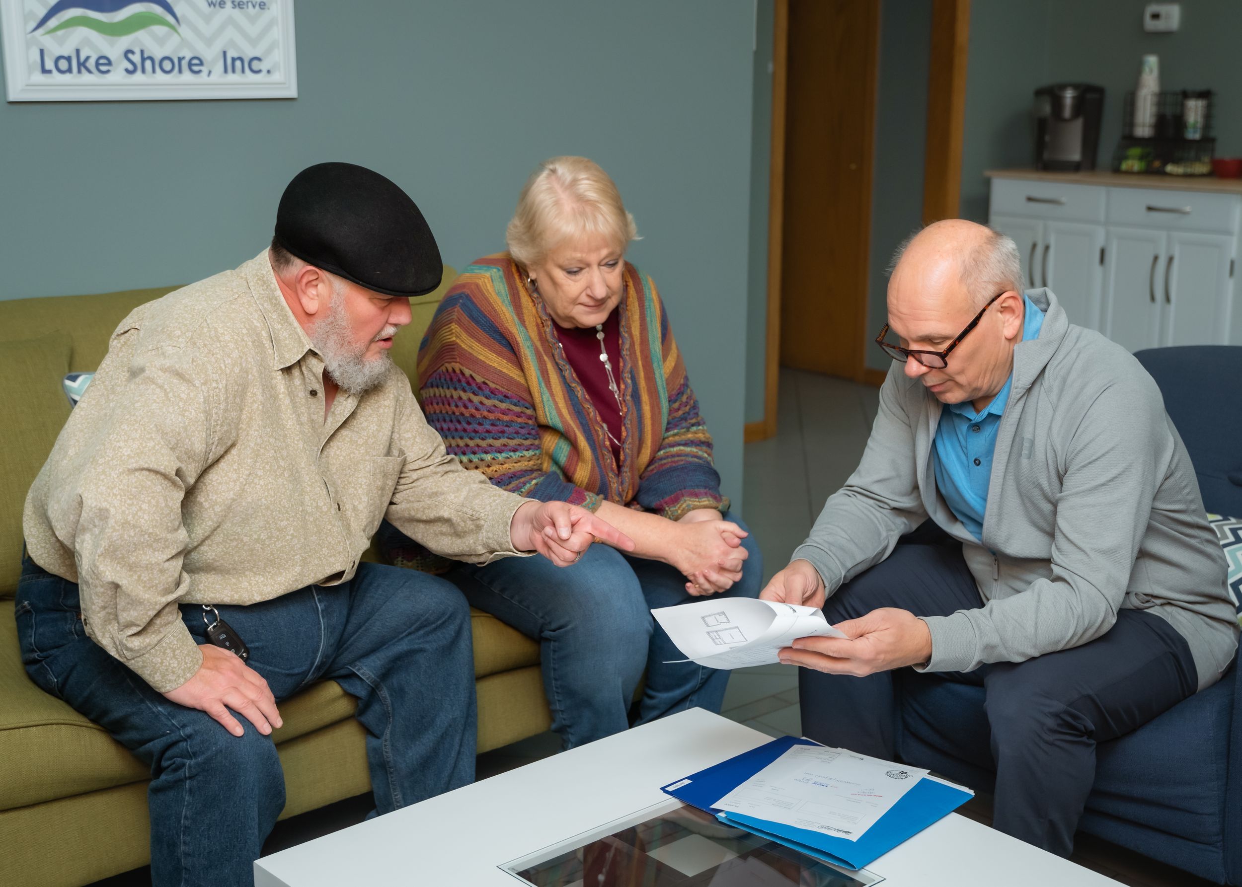 Three people sit together reviewing paperwork and documents at a small table in an office setting.