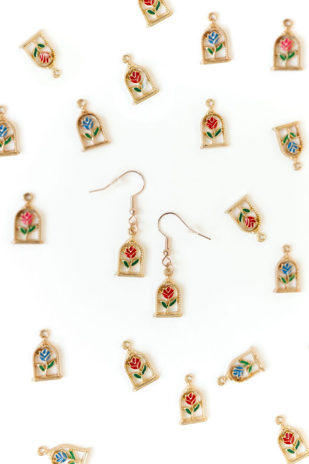 Pattern of small gold earrings with painted floral designs on white background.