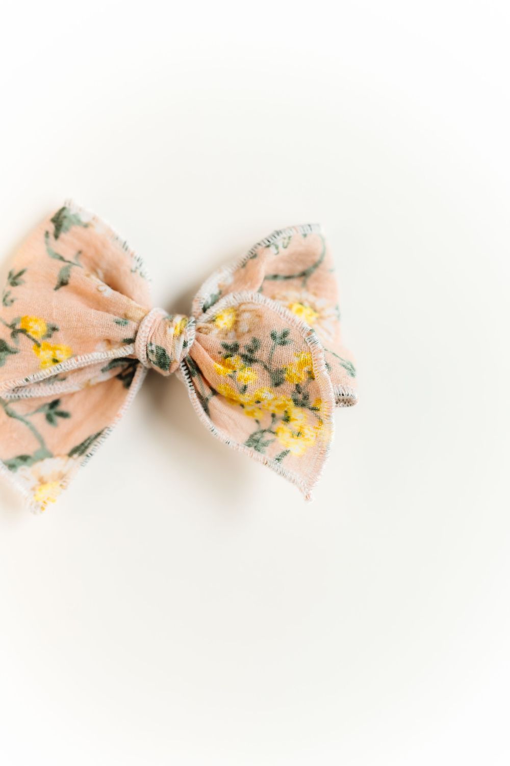 Peach-colored fabric bow with yellow and green floral pattern on white background.
