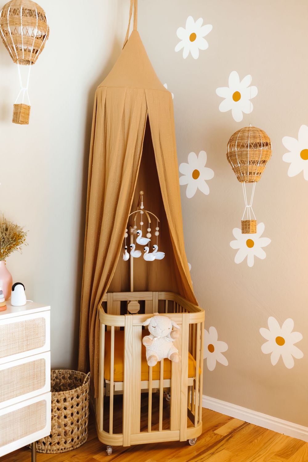 Nursery room with beige canopy, white furniture, and daisy wall decals.