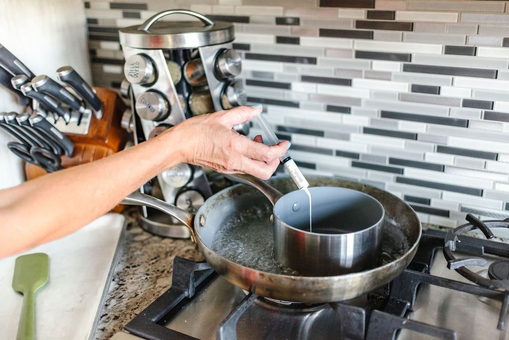 Hands stirring ingredients in a pan on a modern stovetop with tiled backsplash.
