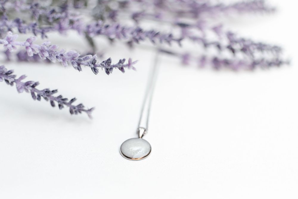 Silver pendant necklace displayed with purple lavender sprigs against white background.