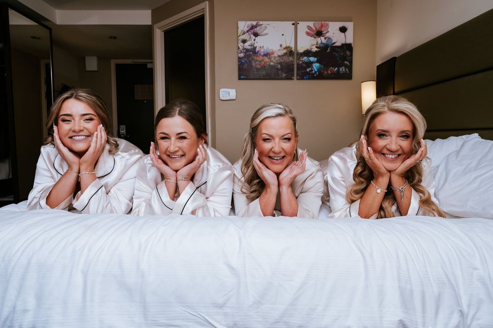 A group of people wearing white robes smile while lying together on a white bed.
