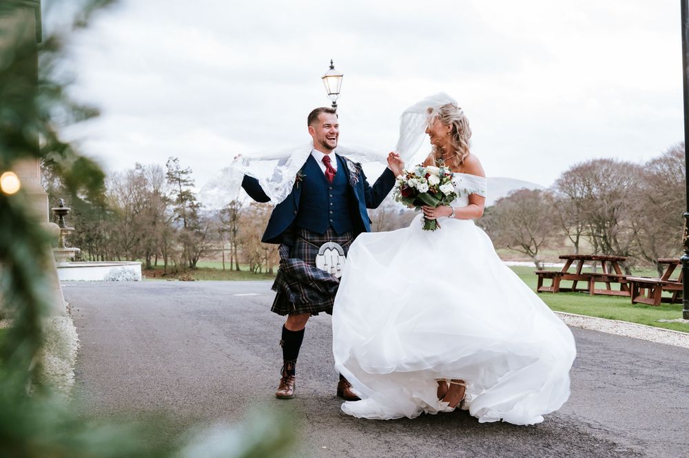 Newlyweds walking hand in hand along a scenic pathway with rustic wooden benches nearby.