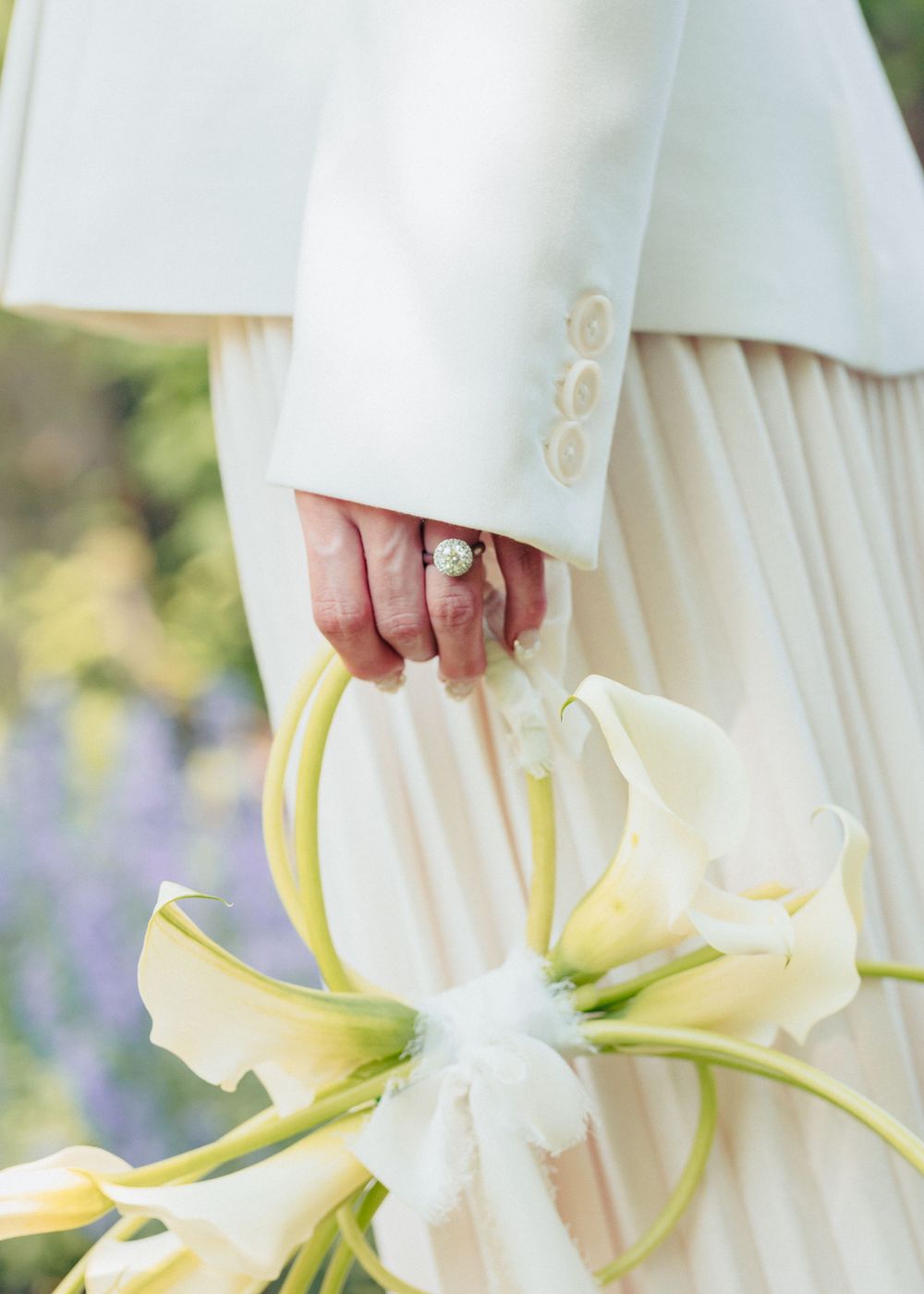 Detail shot of white sleeve with engagement ring and calla lily bouquet.
