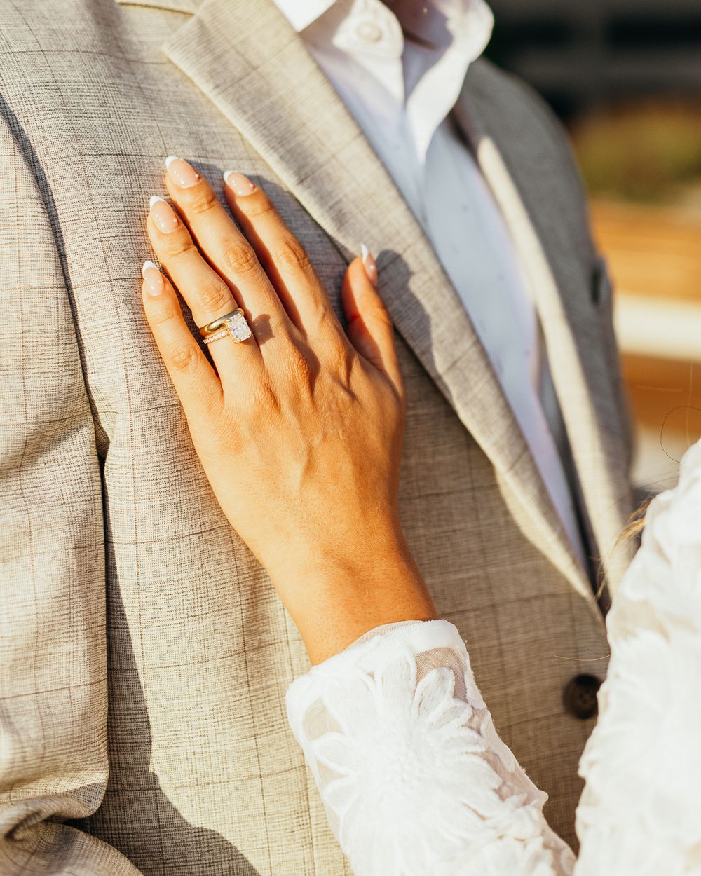 Close-up detail shot of hands resting on a beige suit jacket showing a wedding ring.