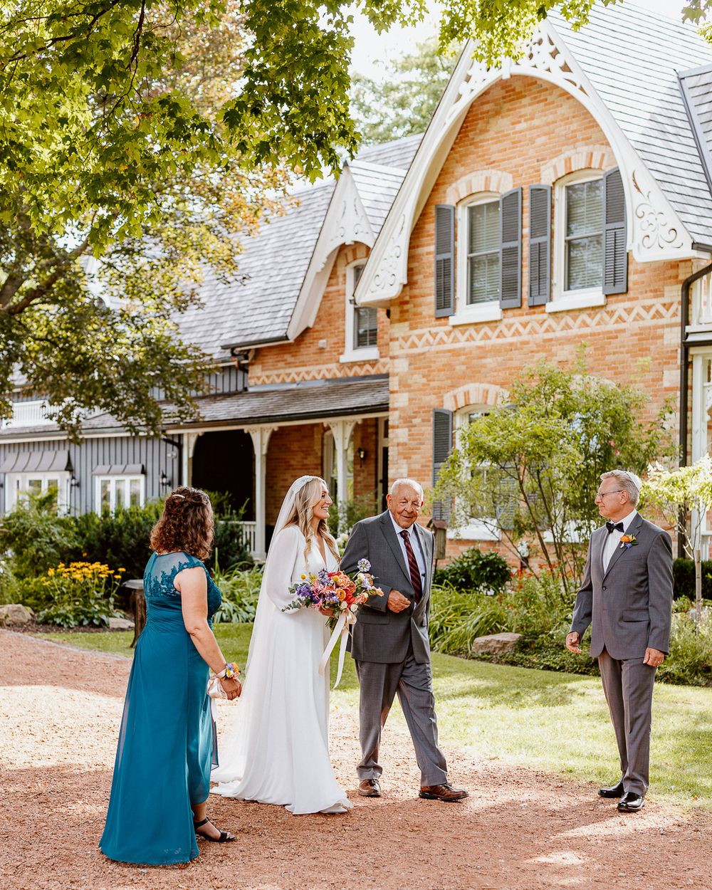 Wedding group arranges for formal photographs outside historic brick building with white trim.