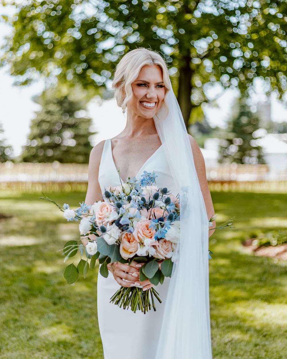 Radiant bride in white gown holding pastel bouquet outdoors.
