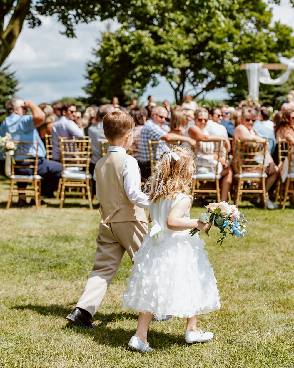 Young flower girl and ring bearer walking down outdoor wedding aisle.
