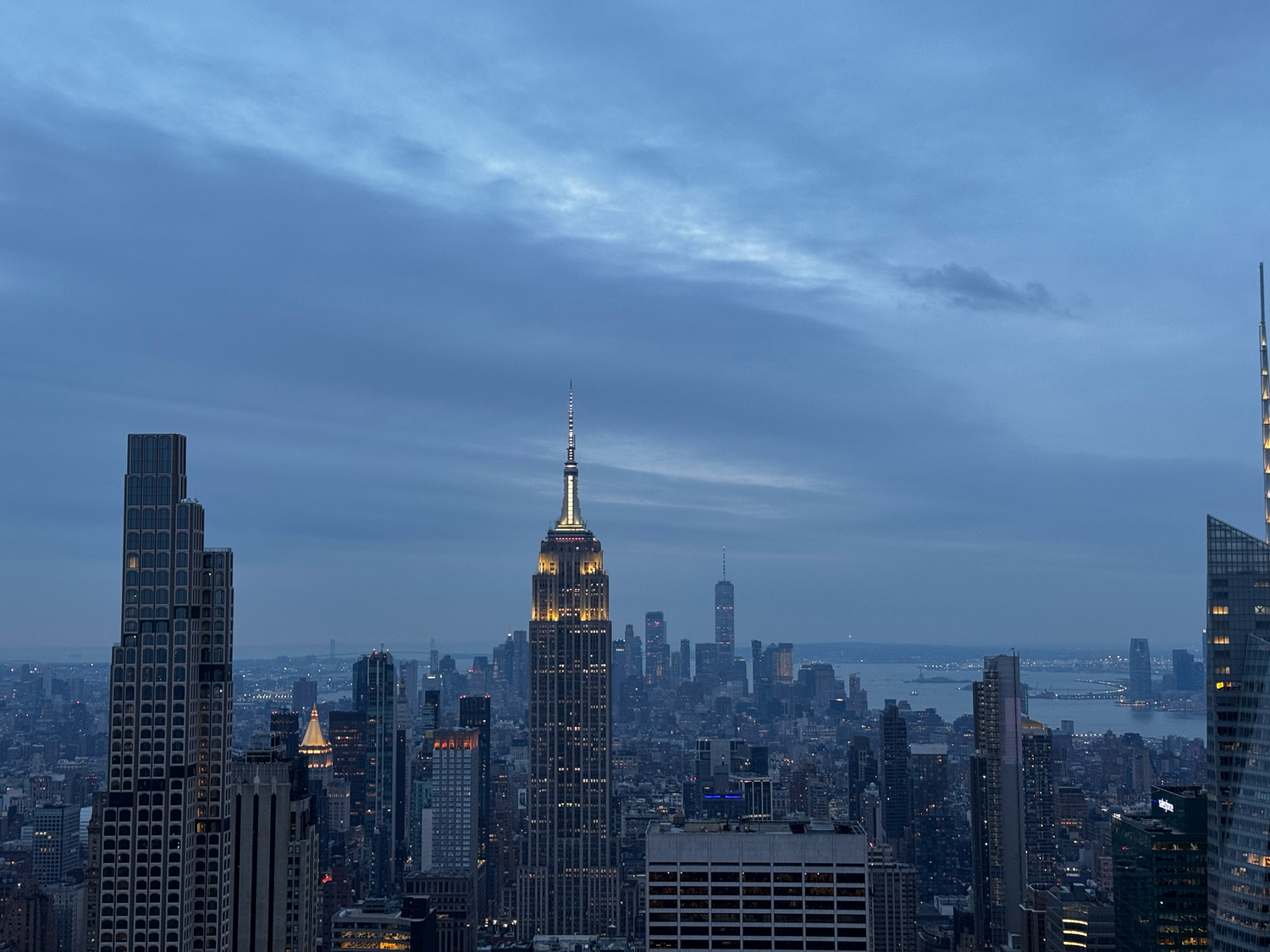Illuminated Empire State Building and Manhattan skyline at dusk with moody blue clouds over New York City.