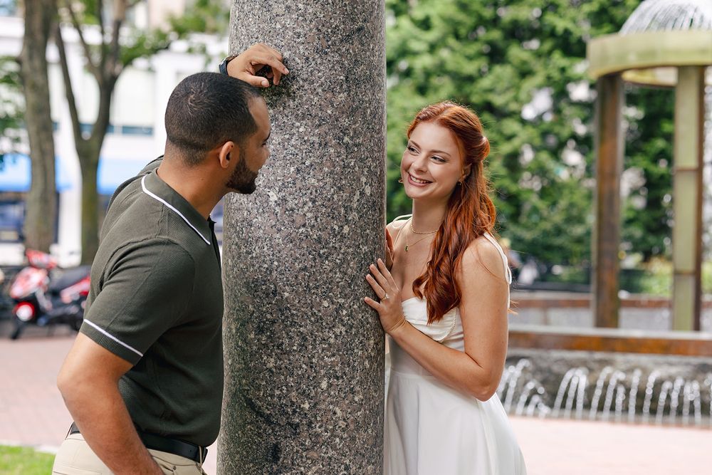 A couple shares an intimate moment while dancing together in a park setting with trees in the background.