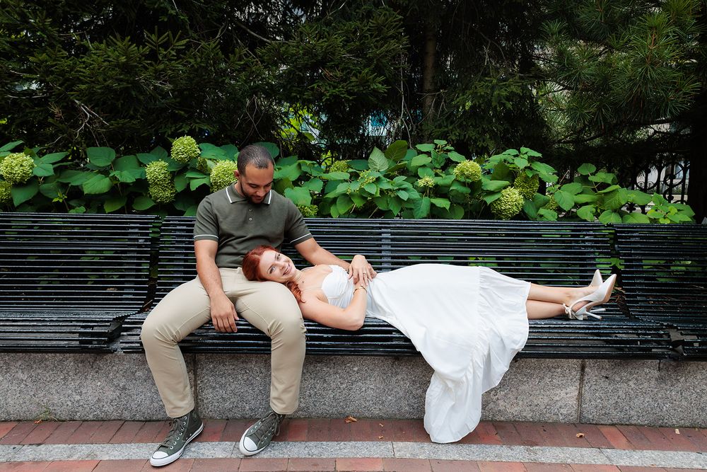 A couple relaxes together on a park bench with lush hydrangea bushes in the background.