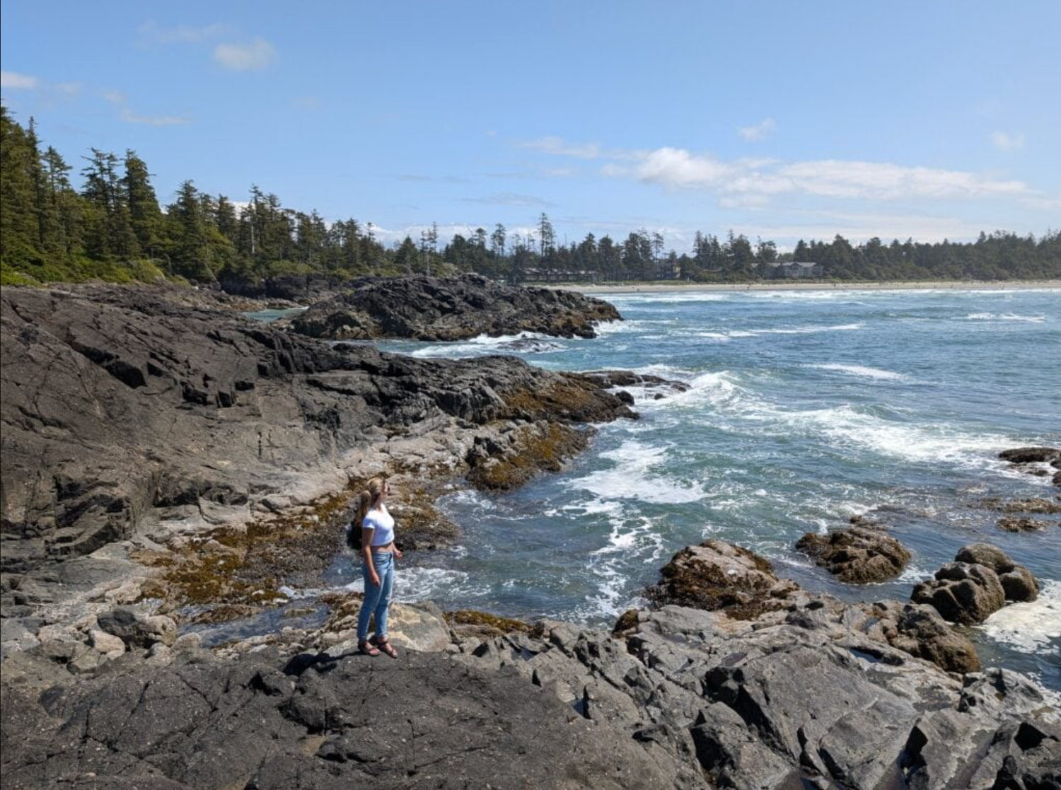 woman stands on rocky point over ocean at Cox Bay Beach in Tofino