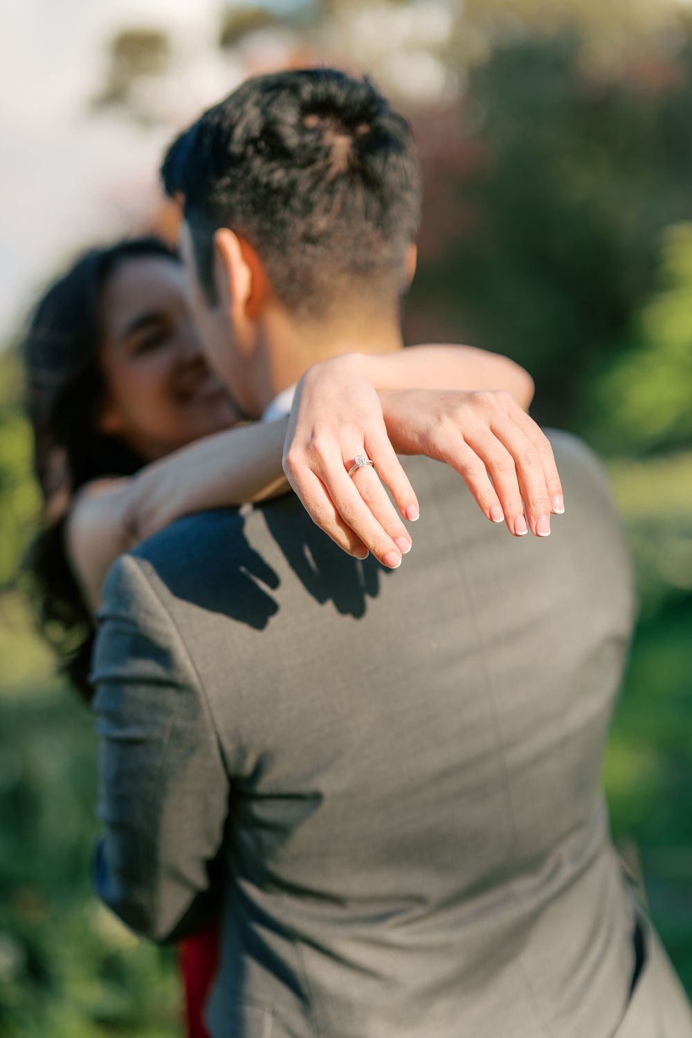 A close-up shot of hands embracing during a romantic moment outdoors, with one person wearing a gray suit.